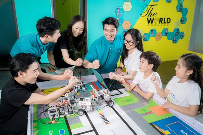 Happy group of Vietnamese children gathered around a table learning robotics engineering from TEKY team members.